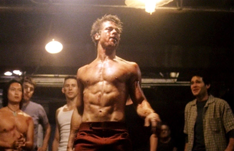 A shirtless man standing in front of a group of people.