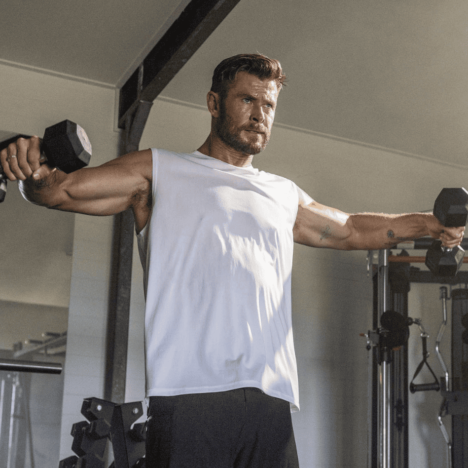 Chris hemsworth lifting dumbbells in the gym.